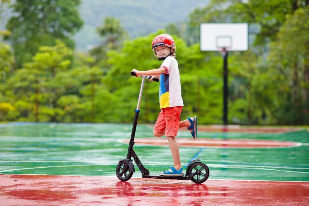 Egy gyermek rollerrel játszik szabadtéri sportpályán