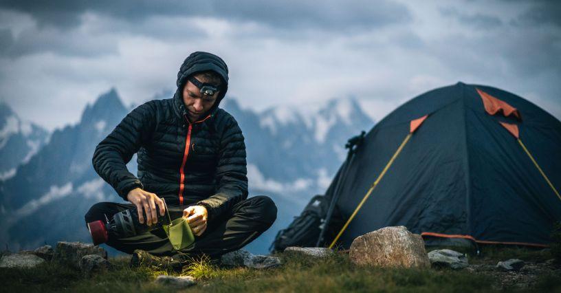 Személy egy sátor mellett ül, túrafelszerelést használva