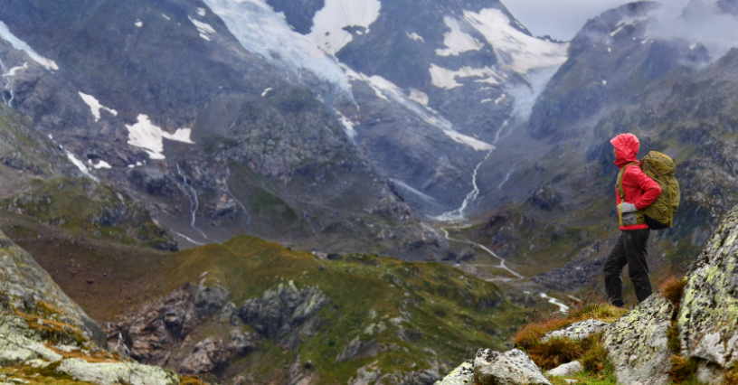 A túrázó megáll a hegyi ösvényen, szemben a hófödte csúcsokkal