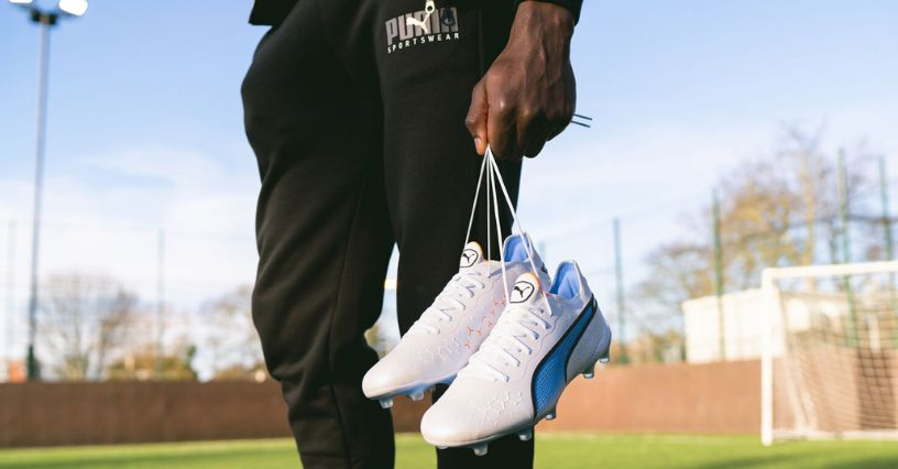 Egy sportoló fehér focicipőt tart a pályán