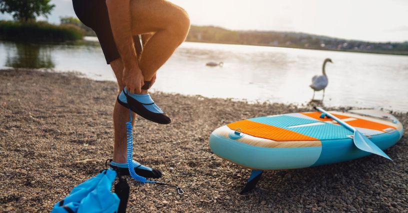 Férfi vízi cipőt visel a parton egy sup mellett