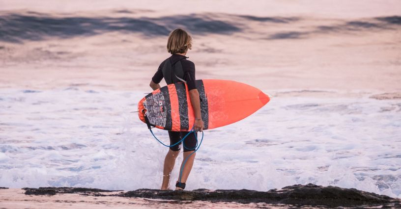 Gyermek áll a vízben szörfdeszkával a kezében
