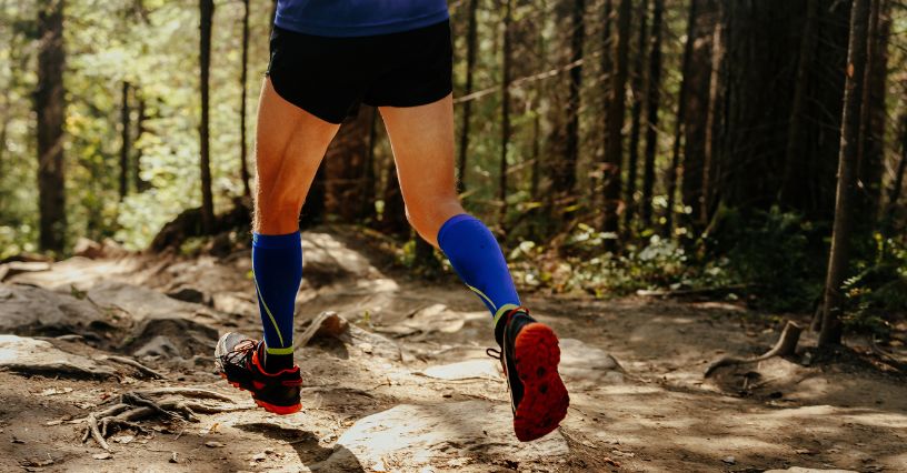 Egy futó kék kompressziós zokniban erdei ösvényen halad